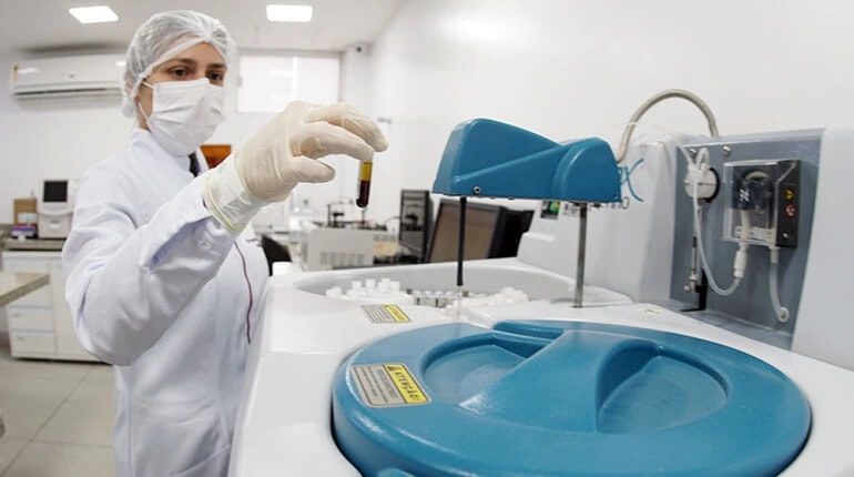 Profissional de laboratório manuseando um tubo de amostra de sangue junto ao analisador